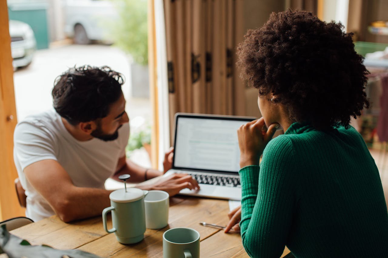Two adults discussing work at home, using a laptop and enjoying coffee.